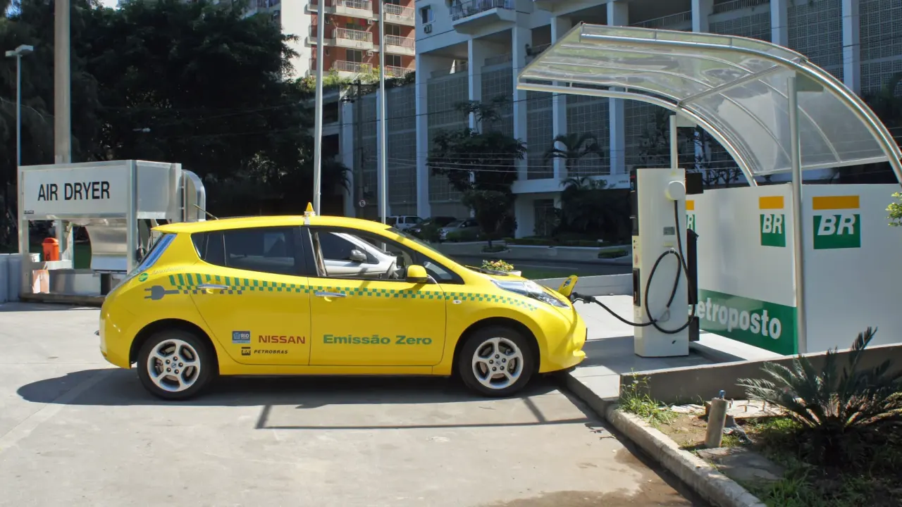 Pesquisa sobre carro elétrico: Nissan Leaf amarelo, táxi com emissão zero, sendo carregado em eletroposto BR no Rio de…